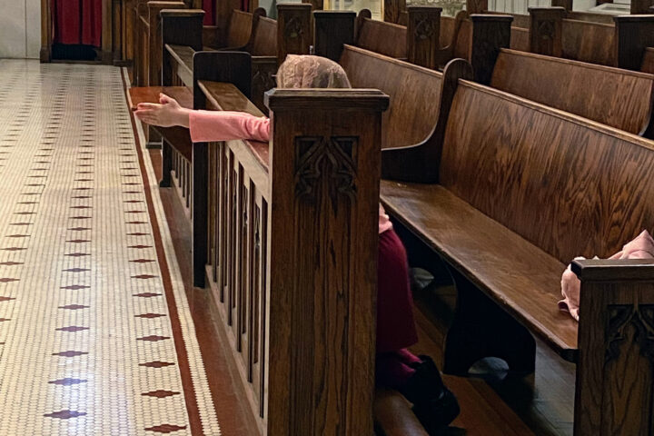 A young girl wearing a veil kneels in a cathedral praying